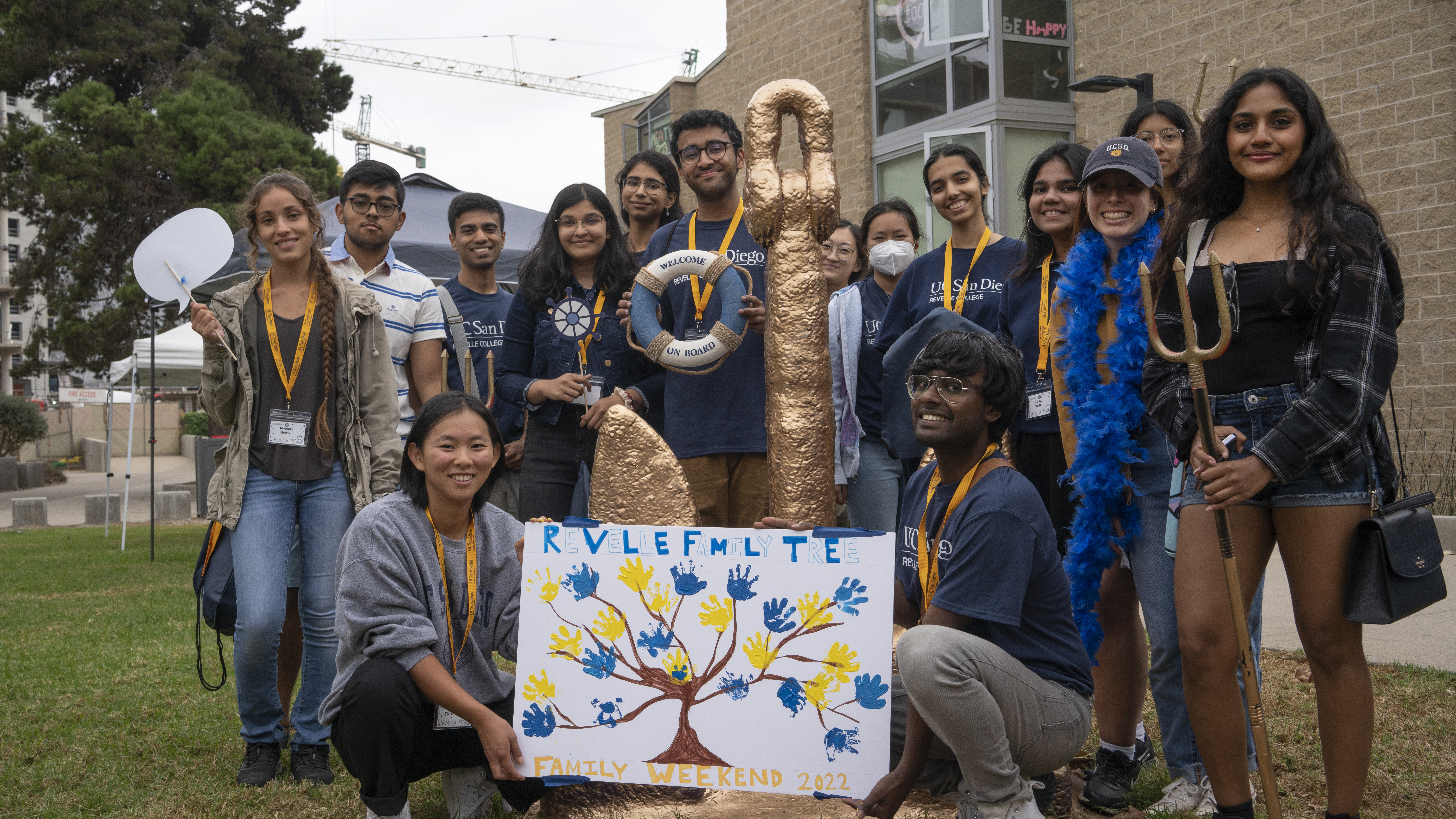 group of smiling students around Revelle anchor with family weekend poster